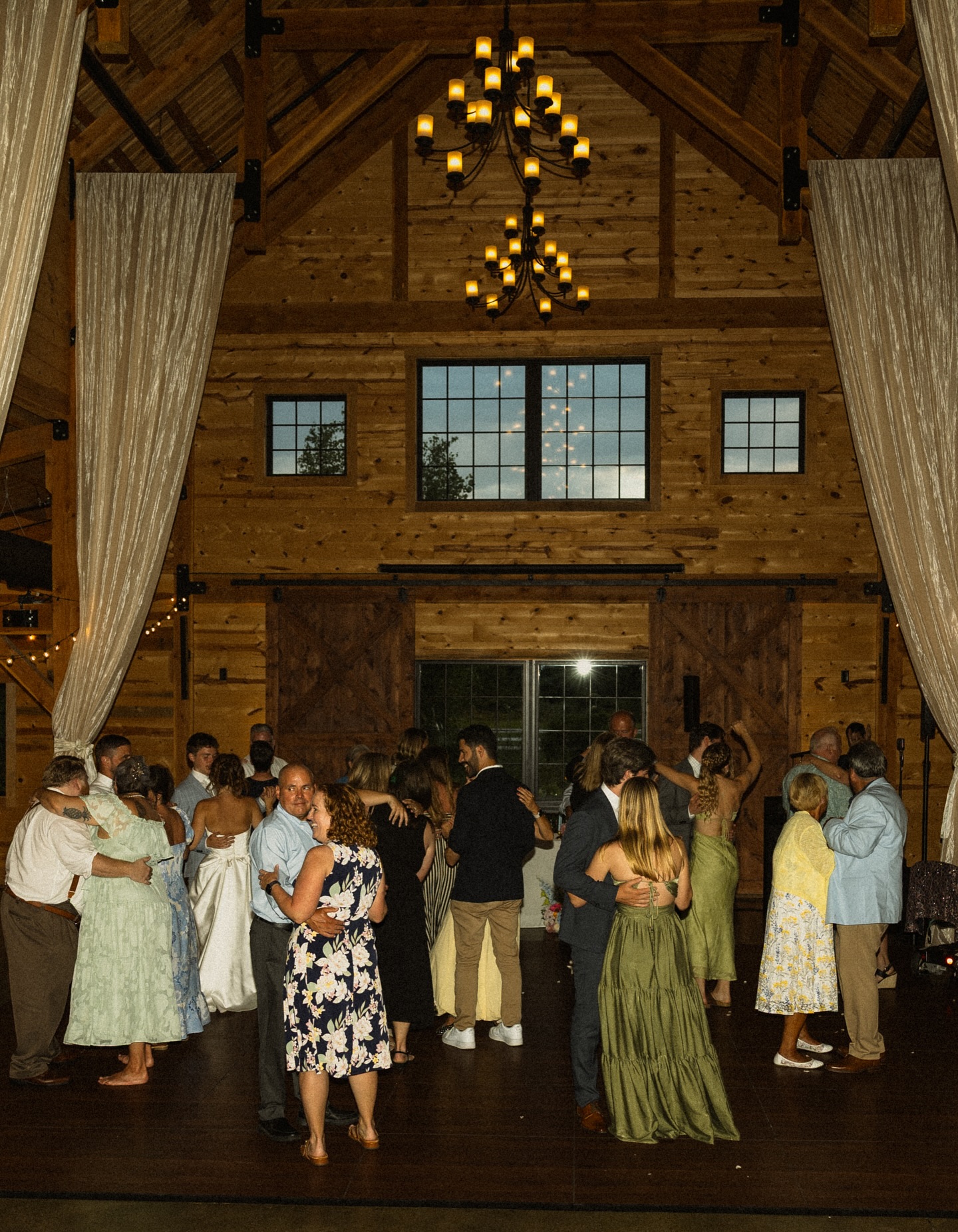 Couples slow dancing beneath the chandeliers at The Barn at Bull Meadow
